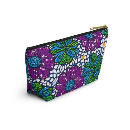 A zippered cosmetic travel bag featuring a bold floral pattern with large purple and blue flowers, green leaves, and white dotted background. This T-bottom pouch stands upright against a white backdrop, evoking African-inspired patterns.