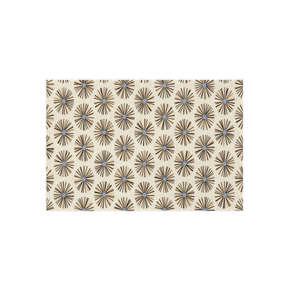 A rectangular beige rug with a repeating geometric pattern of radial black lines forming starburst shapes, each with a small blue dot at the center. This African-inspired outdoor rug is made from weather-resistant polyester chenille for lasting beauty.