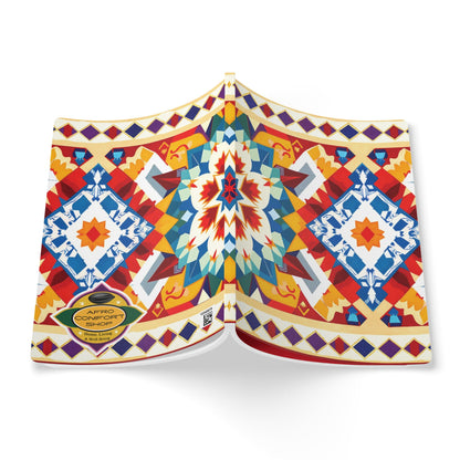 A vibrant African-inspired journal with a geometric, multicolored cover in red, blue, yellow, and white. Diamond shapes and symmetrical motifs stand out, and a gold Afro Comfort seal accents the bottom left. The book is shown open, facing down.