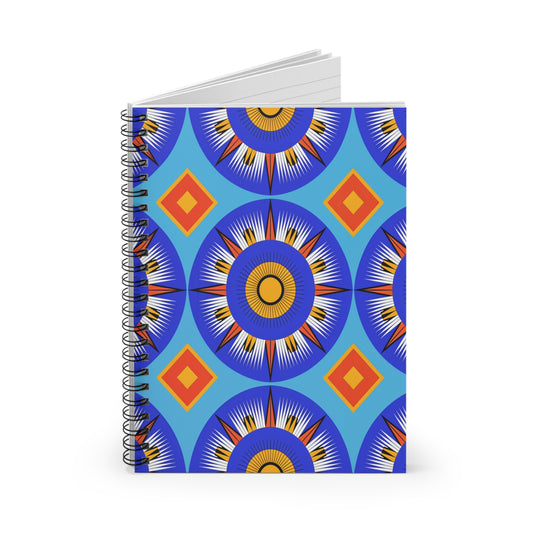 A spiral-bound notebook with a vibrant cover design featuring culturally inspired mandala-like patterns and orange-red diamond shapes on a blue background. The notebook stands upright, offering a premium writing experience with its slightly open pages.