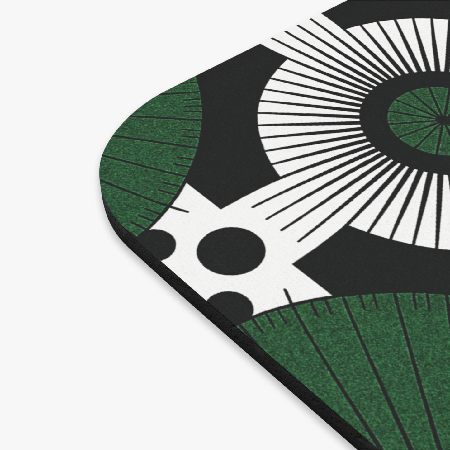 A close-up of the corner of an African mouse pad, a culturally rich desk accessory, featuring a bold, abstract design with black, white, and green colors—radiating lines, concentric circles, green arcs, and large black dots on a white background.
