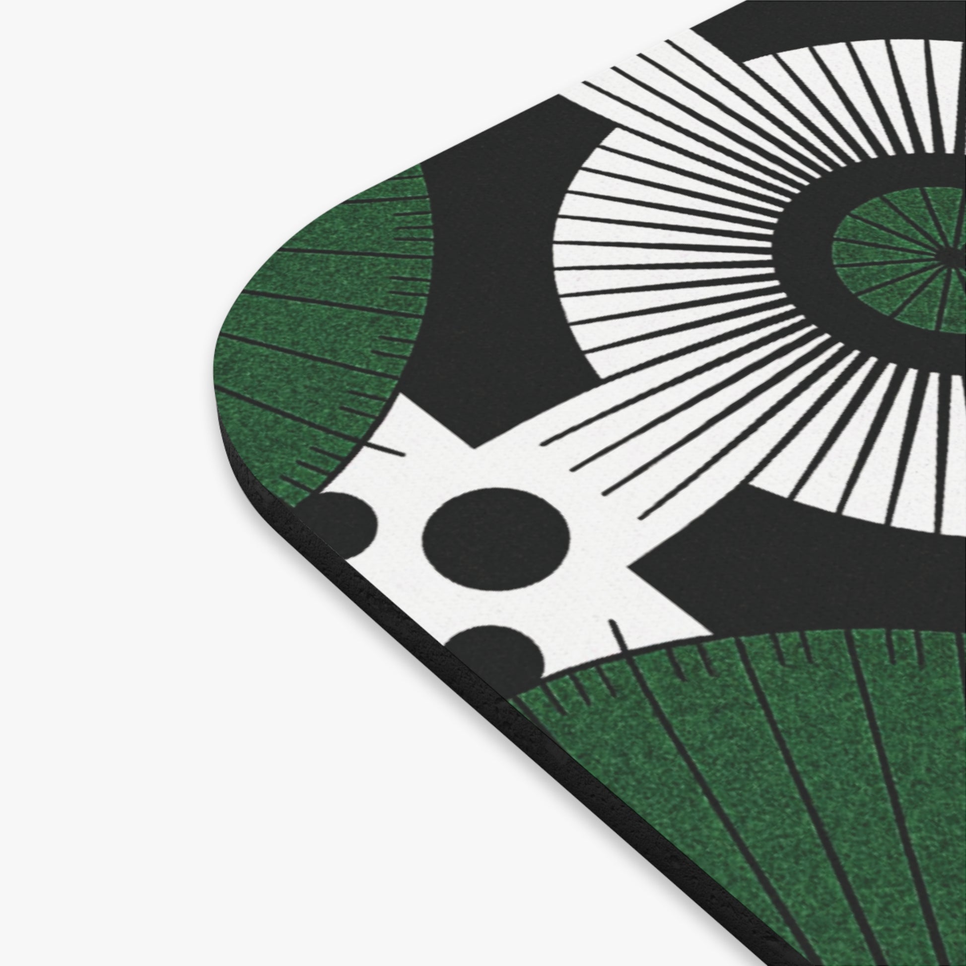 A close-up of the corner of an African mouse pad, a culturally rich desk accessory, featuring a bold, abstract design with black, white, and green colors—radiating lines, concentric circles, green arcs, and large black dots on a white background.