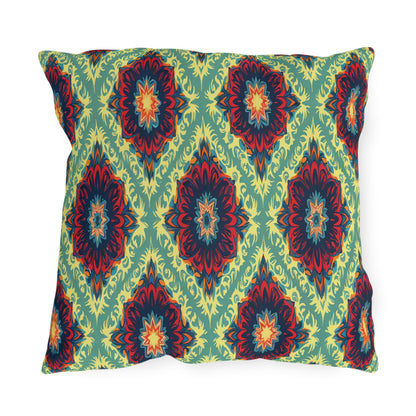 Square pillow with a green background features a symmetrical, bold African-inspired ikat pattern in red, yellow, dark blue, and orange. The design forms diamond shapes with intricate, layered, floral-like centers evenly spaced across the pillow’s surface.