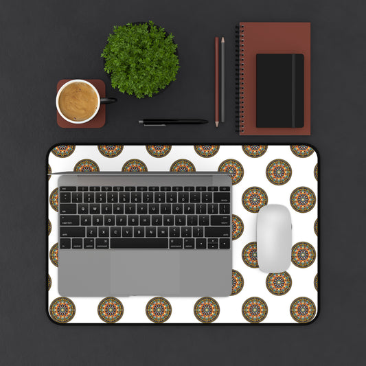 A top view of a desk with a laptop, mouse, and coffee on a colorful workspace accessory—a white Neoprene desk mat with circular mandala patterns. Nearby are a green potted plant, two pencils, a black pen, and stacked brown notebooks on a dark surface.