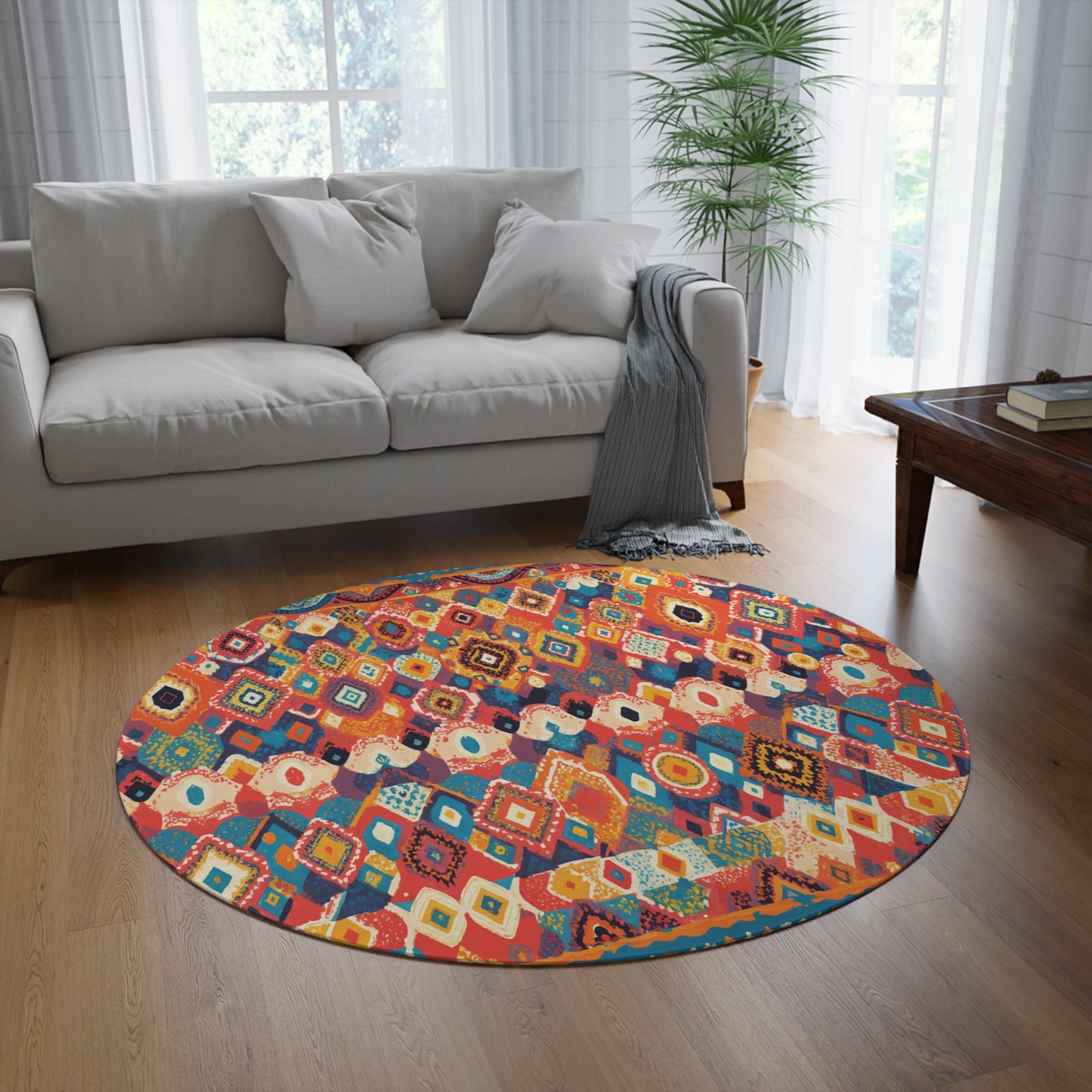 A cozy living room with a light gray sofa, gray throw blanket, and wooden coffee table features a vibrant round rug with geometric patterns in red, yellow, blue, and orange. White curtains and a green plant complete the bright space.