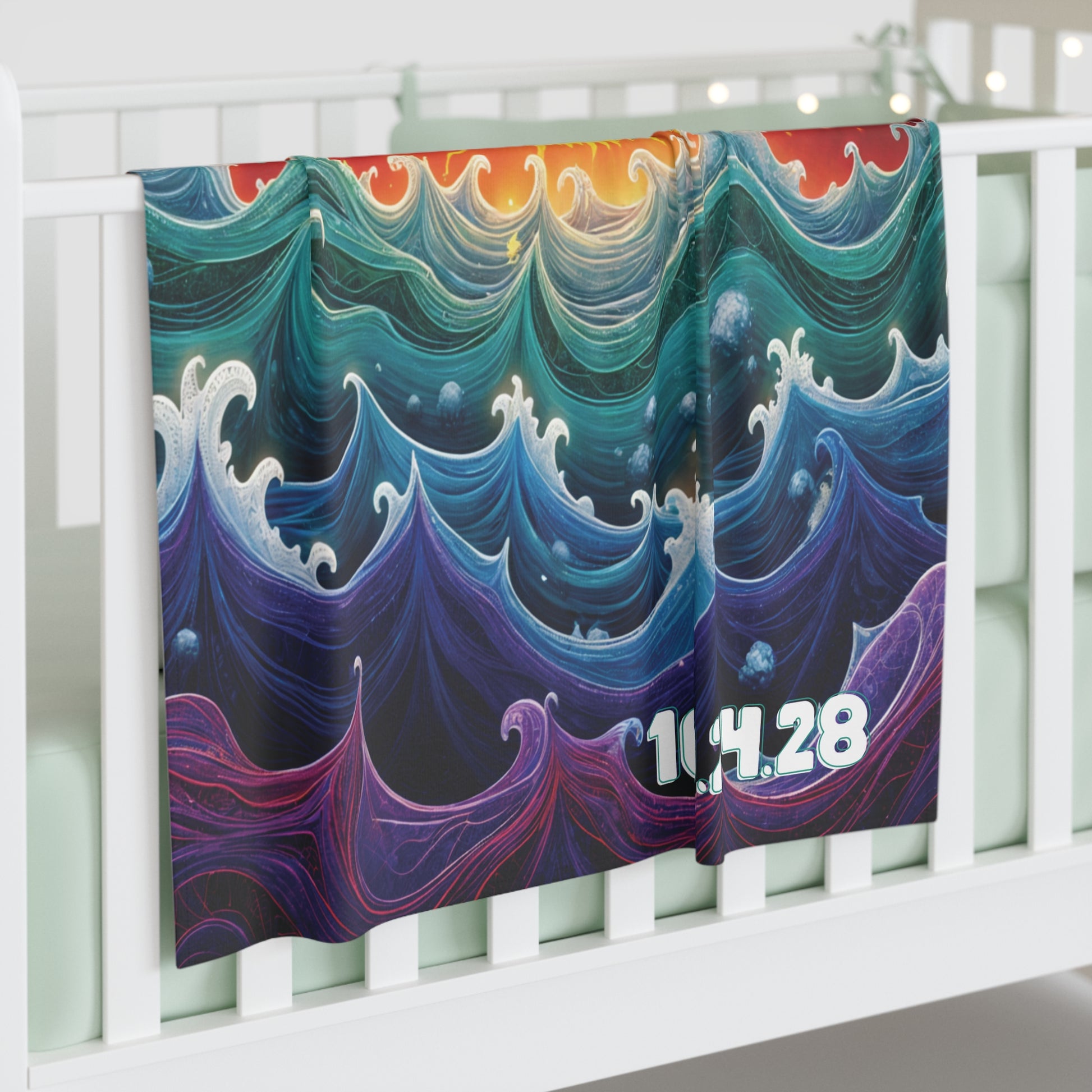 A colorful, personalized baby blanket with swirling, African-inspired decor in blue, teal, and purple hangs draped over a white crib rail. The numbers 10.4.28 appear in the corner, with soft string lights blurred in the background.