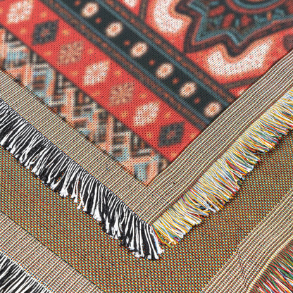 Close-up of two overlapping woven textiles with fringed edges. The top fabric features an African-inspired geometric red, black, and cream pattern; the bottom is brownish with multicolored threads. Both display decorative, multicolored fringe and clearly visible textures.