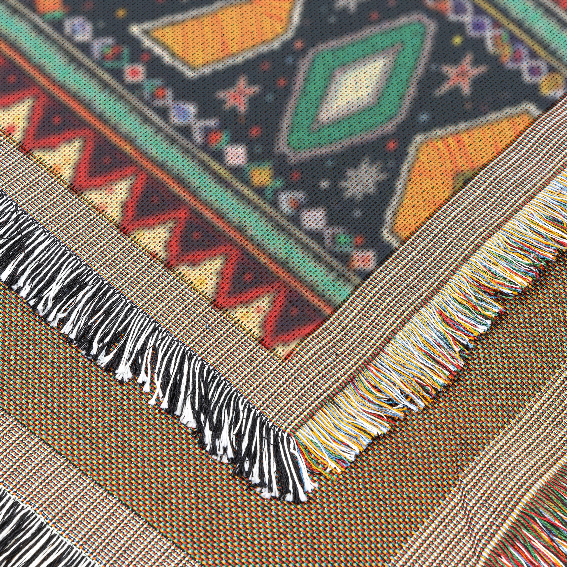 Close-up of a colorful, African-inspired woven textile with geometric patterns in green, orange, red, and black. The fabric edge features multicolored fringe tassels, while overlapping sections show intricate designs typical of traditional weaving.