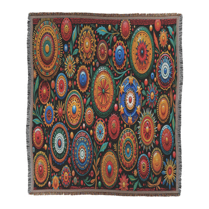 A woven blanket featuring a vibrant pattern of multicolored, circular floral designs in red, yellow, orange, green, and blue on a black background with leafy accents and a subtle patterned border. The cozy weave is finished with fringed edges.