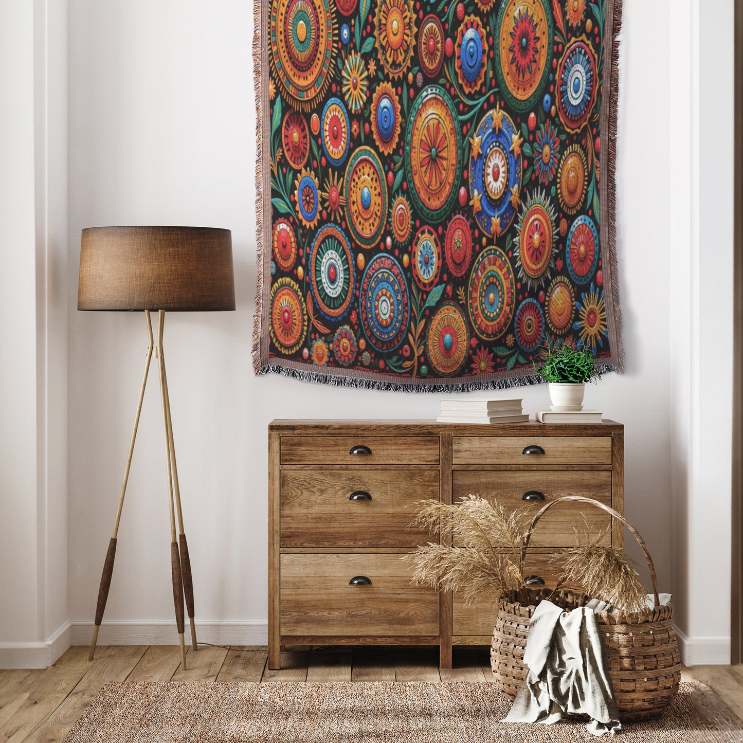 A cozy room features a wooden dresser with a potted plant, a wicker basket of dried grasses, a tripod floor lamp, and a vibrant West African print textile hanging on the wall above the dresser.
