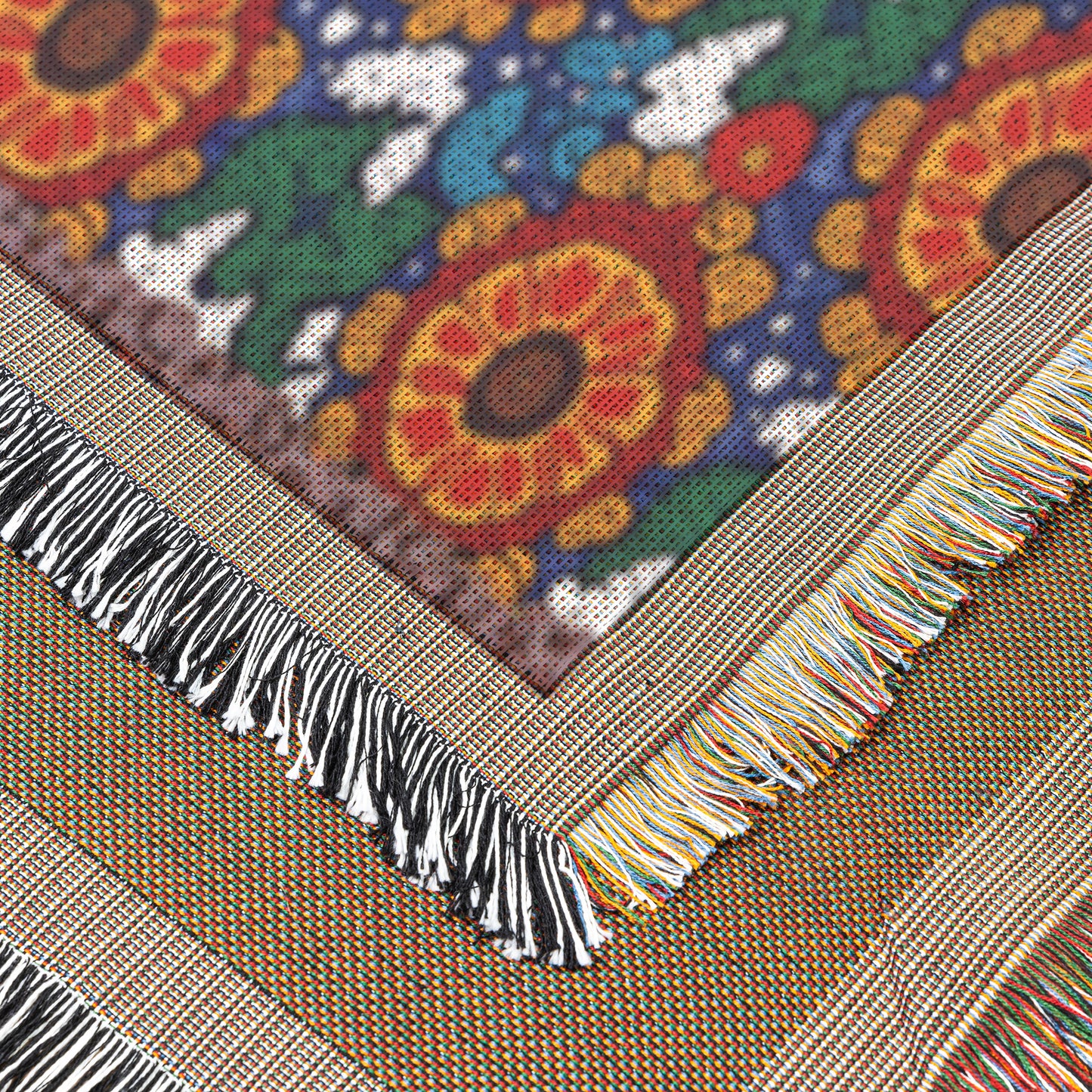Close-up of two overlapping woven textiles. One features an African-inspired floral pattern with sunflowers and abstract shapes, finished with multicolored fringes. The other has a subtle striped design and black-and-white fringes. Textures and weave detail are clearly visible.