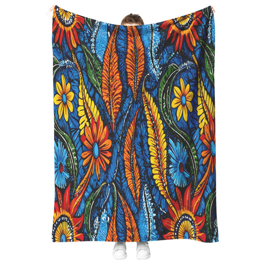 A person, mostly hidden, holds up a colorful African-inspired fabric featuring a bold, vibrant floral pattern with orange, yellow, and red flowers, green leaves, and blue background swirls. Only their shoes and part of their head peek out above and below the fabric.