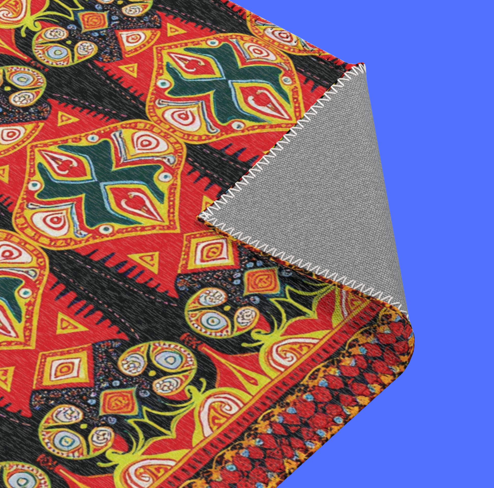 A vibrant, stylish colorful rug features an African-inspired geometric pattern in red, yellow, green, and black. The corner is turned up, revealing a gray underside with white zigzag stitches against a solid bright blue background.