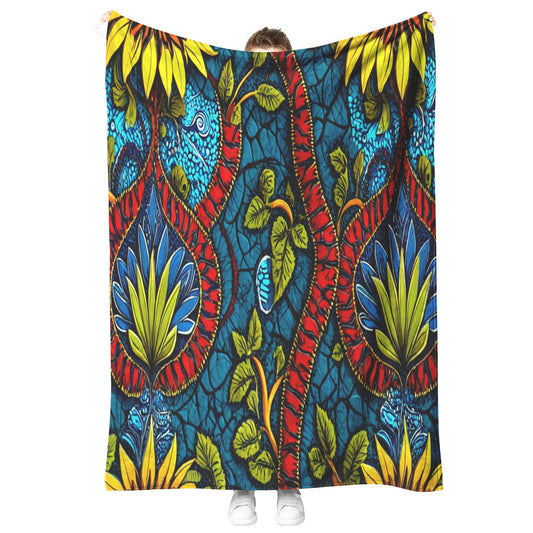 A person stands holding up a vibrant, patterned fabric reminiscent of African-inspired fleece blankets. The fabric features bold, symmetrical designs in yellow, red, blue, and green against a cracked blue backdrop. Only the shoes and part of their head are visible.