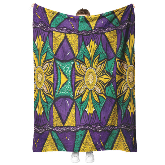 A person stands holding up a large, colorful African-inspired fleece blanket with vibrant geometric and floral patterns in yellow, green, and purple. White sneakers peek out at the bottom, while the person’s face remains hidden behind the stylish microfiber fleece.