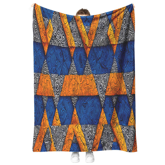 A person stands holding up a large African-inspired blanket with a geometric pattern of blue, orange, and black triangles filled with swirling woodgrain and spiral designs; only their hands, part of their head, and white shoes are visible behind the blanket.