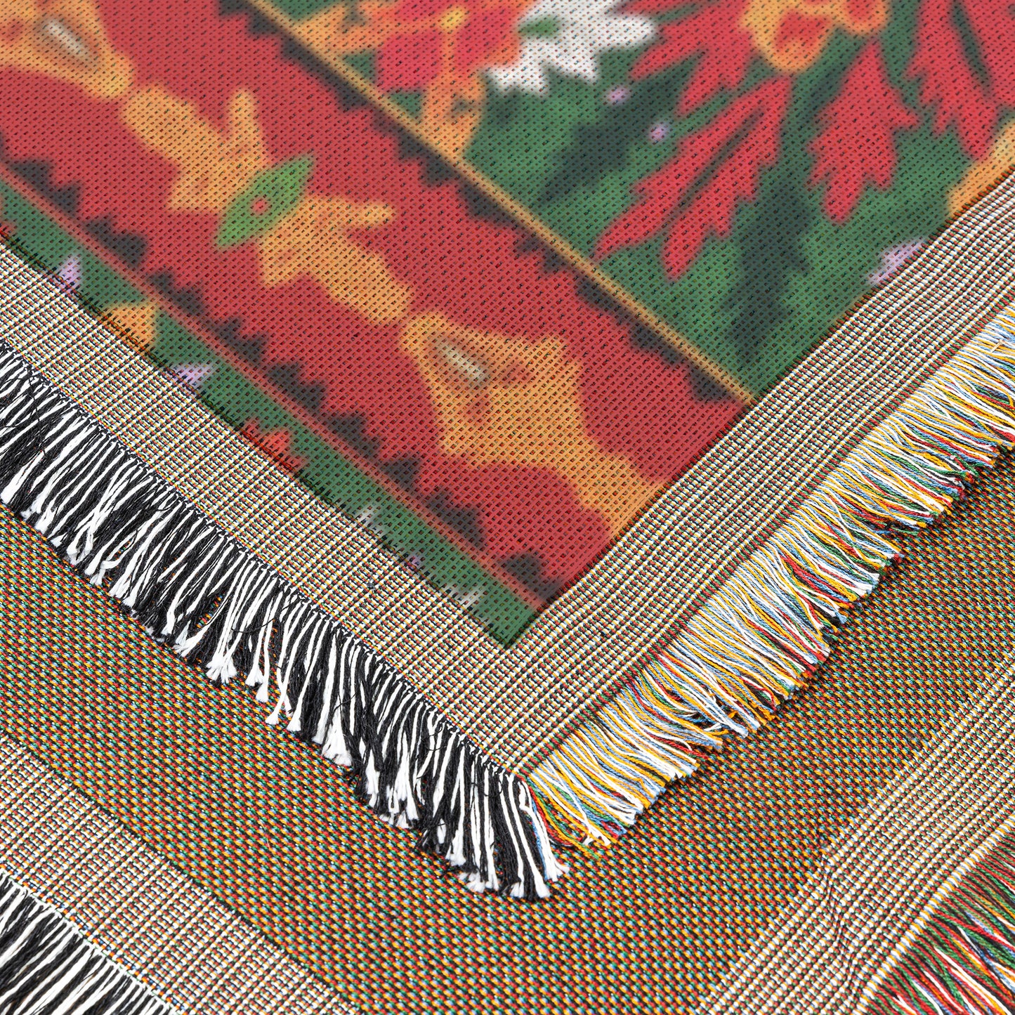 Close-up of an African-inspired woven textile with a colorful floral pattern in red, green, yellow, and white. Two fringed edges cross at an angle—one black and white, the other multicolored—with fabric texture and fibers clearly visible.