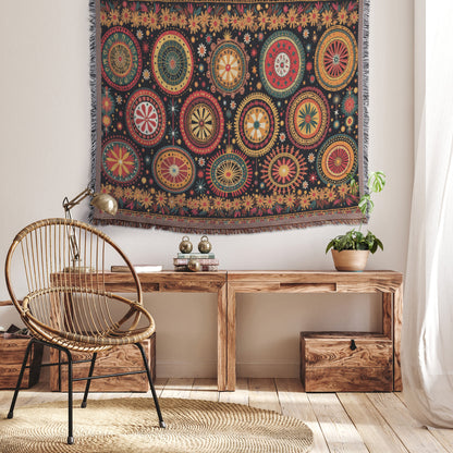 A cozy room with a woven chair, a wooden bench with plants and books, and a vibrant throw blanket complementing the colorful textile wall hanging. Light streams in from a sheer curtain, creating a warm, inviting atmosphere.