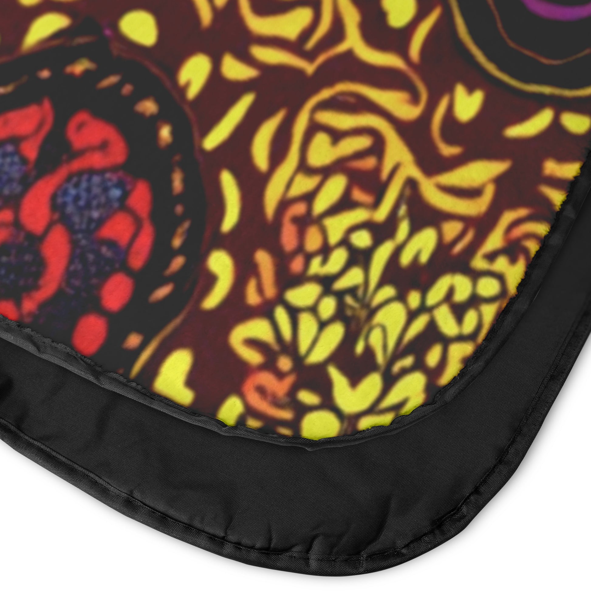 Close-up of a colorful fabric corner with a black edge. The fabric features African-inspired patterns in yellow, orange, red, and purple on a dark background, with organic shapes and swirling lines reminiscent of botanical designs.
