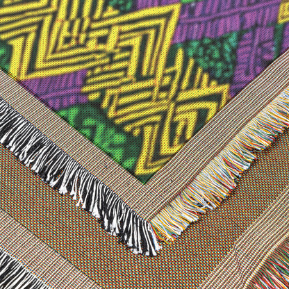 Close-up of a vibrant throw blanket featuring geometric yellow, green, and purple West African print patterns. Two beige fringed edges with multicolored threads highlight the fabric’s bold texture and decorative borders.